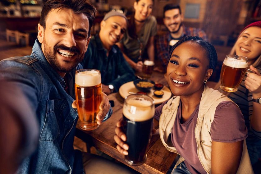 Group of happy friends having fun while drinking beer and taking selfie in a bar.